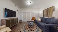 This single-story residence offers a thoughtfully designed layout that balances comfort and functionality across its key living spaces. The living room serves as the heart of the home, featuring wood-look plank flooring, a textured ceiling, and a pair of glass-paneled doors that lead to a private patio, allowing natural light to filter into the space. The room comfortably accommodates a seating area centered around a bold, patterned area rug.

The kitchen is well-equipped with stainless steel appliances, including a refrigerator, electric range, and over-the-range microwave. Cream-toned cabinetry with matte black hardware is complemented by a white subway tile backsplash and light countertops. A peninsula with bar seating provides an additional dining option and casual gathering space, with pendant lighting overhead.

The primary bedroom features plush carpeting and ample room for a full bedroom suite, while the secondary bedroom includes carpeting and space for both sleeping and a dedicated workspace. Each bathroom reflects a consistent design language, with taupe cabinetry, white countertops, and wood-look flooring. The primary bath features a generous vanity with multiple drawers, while the secondary bath includes a full tub-shower combination.