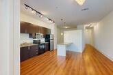 Located at 2115 Piedmont Rd NE in Atlanta, GA, this single-floor unit offers a well-designed open layout that seamlessly connects the kitchen and living area. Rich hardwood flooring runs throughout the main living spaces, lending warmth and continuity to the interior. The kitchen is appointed with dark espresso cabinetry, granite countertops, and a full suite of stainless steel appliances, including a refrigerator, electric range, microwave, and dishwasher. A peninsula with a granite countertop extends into the living area, creating a convenient breakfast bar while defining the kitchen space. Pendant lighting and track lighting illuminate both the kitchen and living areas, complementing the natural light that filters in through large windows with views of surrounding greenery. A bright hallway connects the main living space to the bathroom and closet, with the bathroom featuring a dark-cabinetry vanity, a full tub-shower combination, and tile flooring. The living room is anchored by an elegant chandelier and benefits from additional natural light through a glass door. The closet provides practical storage. Clean white walls throughout the space enhance its bright and airy ambiance, making for a comfortable and functional home in the heart of Atlanta.