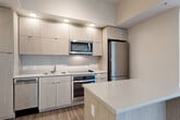 Located at 301 M St SW in Washington, DC, this efficient one-bedroom, one-bathroom unit offers a thoughtfully designed single-floor layout with modern finishes throughout. The entry hallway leads directly into the heart of the home, where the kitchen, dining, and living areas flow together in an open-concept arrangement. The kitchen is well-appointed with light wood-grain cabinetry extending to the ceiling, a full suite of stainless steel appliances including a refrigerator, oven, microwave, and dishwasher, and a light-toned countertop peninsula that provides additional workspace and a natural divider between the kitchen and living area. Wood-look flooring runs throughout the main living spaces, adding warmth and visual continuity. The living area benefits from a striking corner window configuration fitted with roller shades, allowing for abundant natural light and outdoor views of the surrounding greenery. The bedroom is a calm, well-lit space featuring a large window with sheer roller shades that filter natural light softly. Two closets provide ample storage. The bathroom is clean and contemporary, featuring large-format tile flooring, a tub-shower combination with white tile surround, a floating wood vanity with an integrated white sink, and polished chrome fixtures. An in-unit laundry area adds everyday convenience to this well-organized Washington, DC residence.
