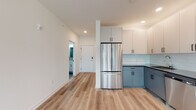 This thoughtfully designed single-floor unit offers a clean, contemporary aesthetic defined by crisp white walls, light-toned luxury vinyl plank flooring, and an abundance of natural light. The open-concept layout connects the kitchen and living area seamlessly, creating a spacious and functional flow. The kitchen is a standout feature, showcasing two-tone cabinetry with soft blue-gray lower cabinets and white upper cabinets, a light blue subway tile backsplash, dark countertops, and a full suite of stainless steel appliances including a French door refrigerator, electric range, over-the-range microwave, and dishwasher. Recessed lighting overhead adds a polished finish to the space. The living area is generously proportioned, with large windows fitted with roller shades that invite natural light and offer open outdoor views. A wall-mounted HVAC unit ensures year-round comfort. The entryway features an electrical panel access point and leads directly to the main bathroom, which includes large-format tile, a white vanity with an undermount sink, and a glass-enclosed walk-in shower with grab bars. A second bathroom offers similar clean finishes with a toilet and vanity. The bedrooms are bright and well-sized, each benefiting from multiple windows with exterior views and hard-surface flooring throughout.
