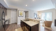 This single-floor residence at 4900 Gender Rd in Columbus, Ohio offers a thoughtfully designed open-concept layout with modern finishes throughout. The kitchen is a standout feature, showcasing rich dark espresso cabinetry that extends to the ceiling, light granite countertops, black appliances including a refrigerator, range, and built-in microwave, and a large peninsula with bar seating for two — ideal for casual dining and entertaining. Wood-style plank flooring runs through the kitchen and living areas, adding warmth and continuity to the space. The living room is bright and comfortable, with neutral carpet, large French doors that invite natural light and provide access to a private balcony. The bedrooms offer plush carpeting, natural light from windows, and generous closet space, including walk-in and double-door closets with built-in shelving. Two bathrooms serve the unit, each featuring tile flooring, dark vanity cabinetry, and granite-style countertops. One bathroom includes a glass-enclosed walk-in shower, while the other offers a full tub surround. The overall palette of warm neutrals and consistent finishes creates a cohesive, move-in-ready environment throughout the home.