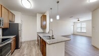 Located at Two Addison Place in Pooler, Georgia, this single-floor residence offers a well-designed, open-concept layout that seamlessly connects the kitchen and living areas. The interior is finished with light wood-tone luxury vinyl plank flooring throughout the main living spaces, contributing to a clean and modern aesthetic.

The kitchen is a functional centerpiece of the home, featuring warm-toned wood cabinetry, granite-style countertops, and a peninsula island with a double stainless steel sink and elegant pendant lighting overhead. Stainless steel appliances — including a refrigerator, electric range, and over-the-range microwave — complete the kitchen's polished look. The open peninsula connects directly to the spacious living area, making it ideal for entertaining.

The bedrooms are carpeted for comfort and include ceiling fans, as well as windows with blinds that allow for natural light and outdoor views of the surrounding neighborhood. Louvered closet doors are featured in the hallway, providing convenient storage access.

The bathroom is finished with granite-top wood vanity cabinetry, a tub/shower combination, and wood-look flooring. A walk-in closet is accessible adjacent to the bathroom, offering generous storage space. Throughout the residence, neutral wall tones and consistent finishes create a cohesive and inviting living environment.