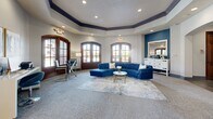 Located at 2201 Orem Dr in Houston, TX, this community clubhouse offers a polished and welcoming environment designed for comfort and functionality. The entrance greets visitors with rich slate tile flooring, soaring ceilings, and a striking cluster of pendant light fixtures, setting an upscale tone from the moment of arrival. Elegant arched doorways and warm wood-framed French doors connect the various areas throughout, creating a cohesive and inviting architectural flow. The main lounge is a standout feature, anchored by an octagonal tray ceiling with navy blue crown molding, recessed lighting, and large arched windows that flood the space with natural light. A bold blue sectional sofa and contemporary furnishings give the room a vibrant, residential feel. Adjacent seating areas offer quieter retreats, including a refined sitting room with a tufted white sectional, decorative mirrors, and a marble-top coffee table. A dedicated business center provides a workstation and seating for residents' everyday needs. The fitness center is well-equipped with cardio machines, a rowing machine, free weights, exercise balls, full-length mirrors, and a wall-mounted TV. Throughout, a cohesive palette of soft gray, crisp white, and deep teal blue ties the entire facility together into a sophisticated and functional community space.