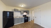 Located at 12702 Blue Ridge Circle in Grandview, Missouri, this single-floor unit offers a clean, updated living environment with a thoughtful layout spread across an open and functional floor plan. The kitchen is a standout feature, equipped with gray shaker-style cabinetry, light granite-look countertops, a white subway tile backsplash, and black appliances including a refrigerator, electric range, and under-cabinet range hood. The kitchen opens directly into the living area, which is finished with durable hardwood-style vinyl plank flooring that runs consistently throughout the space, contributing to a cohesive and modern aesthetic. The living area benefits from natural light via a window fitted with blinds and includes a wall-mounted HVAC unit for climate control. The bedroom is a comfortable, well-sized room with a ceiling fan, a window allowing natural light, and the same hardwood-style flooring. The bathroom features a gray vanity with a white countertop, a framed mirror, and a bathtub, with an adjacent closet providing additional storage. Neutral, light-toned walls throughout the unit create a bright, welcoming ambiance well-suited for everyday living.