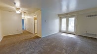 Located at 379 Rivermoor Dr in Marietta, Pennsylvania, this single-floor residence offers a straightforward and functional layout designed for comfortable everyday living. The main living area is generously proportioned, featuring wall-to-wall carpeting that adds warmth underfoot and a neutral color palette throughout that creates a clean, versatile backdrop for any décor style. A standout feature of the living space is the set of elegant French doors, which flood the room with natural light and provide access to the outdoors, enhancing the sense of openness. Ceiling-mounted lighting ensures the space remains well-lit at all times. An open passageway connects the living area to the kitchen, which is visible in the background and features light wood cabinetry and a full-size refrigerator, offering practical storage and cooking space. A hallway extends further into the home, leading to additional rooms, hinting at a well-organized floor plan. The consistent use of light tones on the walls and trim throughout contributes to a bright and airy ambiance across the entire residence. This single-level home provides easy, step-free access and a cohesive flow between its living spaces.
