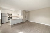 This single-floor unit offers a practical and efficiently designed layout, accommodating four bedrooms and one bathroom within a thoughtfully utilized footprint. The combined kitchen and living area serves as the heart of the unit, where a modern kitchen stands out with crisp white shaker-style cabinetry, speckled quartz countertops, a peninsula for additional workspace, and a full suite of stainless steel appliances including a refrigerator, electric range, and over-the-range microwave. A window with vertical blinds allows natural light to brighten the kitchen area. The living space is open and versatile, featuring light wood-look flooring and neutral warm-toned walls that carry throughout the unit. Each of the four bedrooms is modest in scale, with the primary bedroom offering a dedicated closet featuring double hanging rods for organized storage. The bedrooms are finished with the same wood-look flooring and textured ceilings, creating a cohesive feel. Several rooms feature windows with sheer vertical blinds, inviting natural light and outdoor views. The bathroom is clean and functional, appointed with a full-size soaking tub and shower combination, brushed nickel fixtures, and neutral finishes. The overall aesthetic is fresh, clean, and move-in ready.