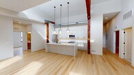This single-floor, 4-bedroom, 2-bathroom residence masterfully combines modern design with industrial character. Light hardwood flooring flows seamlessly throughout, complementing crisp white walls and creating a bright, cohesive aesthetic. Striking exposed timber columns and visible ductwork add warmth and architectural intrigue to the open-concept kitchen and living area.

The kitchen is a standout feature, equipped with stainless steel appliances, floor-to-ceiling white cabinetry with matte black hardware, a white quartz waterfall island, and a classic subway tile backsplash. Three pendant lights anchor the space above the island, while soaring ceilings amplify the sense of openness.

The four bedrooms offer clean, light-filled retreats, several featuring arched black-framed windows that flood the rooms with natural light. The primary bedroom provides generous proportions with direct views into the main living area. A well-lit hallway with a skylight connects the bedrooms, enhancing the airy feel of the layout.

The two bathrooms are finished in a contemporary style, each featuring terrazzo flooring, wood-toned floating vanities, white countertops, and matte black fixtures. One bathroom includes a glass-enclosed walk-in shower with white tile, while the other offers a full soaking tub with warm vertical tile surround.