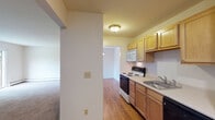 Located at 1187 Hillside Ave in Schenectady, NY, this single-floor unit offers a well-organized layout designed for comfortable everyday living. The kitchen is outfitted with light maple cabinetry, a white electric range, built-in microwave, dishwasher, and a stainless steel sink, all set atop warm hardwood-style flooring. A galley-style configuration keeps everything within easy reach and flows naturally into the adjacent dining and living areas. The main living area is generously proportioned, featuring plush carpeting, neutral walls, and a sliding glass door that opens to a private balcony overlooking lush greenery — allowing natural light to fill the room. Baseboard heating and a wall-mounted air conditioning unit ensure year-round comfort. A pendant light fixture anchors the dining space, which transitions smoothly between the kitchen and living zones. The bedroom is carpeted and quiet, offering a full-width closet with built-in shelving and hanging rods for ample storage. The bathroom is clean and functional, featuring a pedestal-style vanity with a well-lit mirror cabinet. Throughout the unit, a consistent palette of neutral tones and practical finishes creates a cohesive, move-in-ready atmosphere suited to a range of lifestyles.
