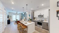 Located at 407 Pratt Ave NE in Huntsville, Alabama, this 2-bedroom, 2-bathroom residence offers a thoughtfully designed open-concept floor plan with contemporary finishes throughout. The kitchen serves as a central focal point, showcasing two-tone cabinetry with white upper cabinets and wood-toned lower cabinets, a chevron tile backsplash, stainless steel appliances, and a large quartz-topped island with a matte black sink and seating for multiple guests — ideal for both everyday living and entertaining. Pendant lighting overhead adds a refined touch.

The living area flows seamlessly from the kitchen and features a distinctive teal accent wall, light wood-look flooring, and access to a private balcony overlooking a landscaped courtyard. The primary bedroom includes a teal accent wall, a ceiling fan, a dedicated closet with built-in wire shelving, and a direct en-suite bathroom. The bathrooms are finished with granite countertops, undermount sinks, and wood-toned vanities. A second bedroom mirrors the comfortable and stylish design language found throughout the home. Two dedicated closets provide ample storage. The overall aesthetic balances modern design with warm, welcoming tones.