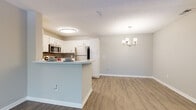 Located at 3643 Huntington Place Dr in Sarasota, FL, this single-story residence offers a well-designed, open-concept layout highlighted by warm wood-look flooring and soft neutral wall tones throughout. The kitchen is a functional centerpiece, featuring crisp white cabinetry, a tasteful gray tile backsplash, stainless steel appliances including a refrigerator, range, microwave, and dishwasher, and a granite-style countertop peninsula that doubles as a breakfast bar. The peninsula seamlessly connects the kitchen to the adjoining dining and living areas, enhancing the open flow of the space. A classic chandelier anchors the dining area, adding a polished touch to the everyday living space. The spacious living area benefits from ceiling fans and provides ample room for comfortable furnishings. A dedicated bedroom features large windows that invite natural light and offer views of surrounding greenery, complemented by a ceiling fan for year-round comfort. The bathroom includes a granite-style vanity countertop with an undermount sink and a shower-tub combination. Throughout the unit, textured ceilings, clean white baseboards, and consistent flooring choices contribute to a cohesive, well-maintained aesthetic suited to Florida living.