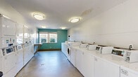 Located at 4960 Edmondson Pike in Nashville, Tennessee, this shared laundry facility offers a well-organized, single-floor layout designed for efficient, community use. The room is generously sized, providing ample open floor space to move comfortably between machines and folding areas.

Rows of white top-load and front-load washing machines line both sides of the room, complemented by a bank of stacked dryers along one wall, offering a substantial number of machines to accommodate high-demand use. A built-in folding counter runs along one wall, providing a convenient workspace for sorting and folding laundry. Additional folding surfaces are available near the entrance area.

The interior features smooth concrete flooring, white-painted walls, and a distinctive teal accent wall at the far end of the room, adding a touch of color to the otherwise neutral palette. Flush-mounted ceiling light fixtures provide consistent, even illumination throughout the space. A window on the teal accent wall allows natural light to filter in, brightening the room during daytime hours.

Informational signage is posted on the walls, and the facility includes a stainless steel waste bin for convenience. The space is clean, functional, and clearly designed to serve a residential community with all the essential amenities needed for on-site laundry.