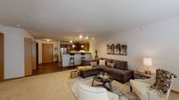 This single-floor residence offers a thoughtfully designed open-concept layout that seamlessly connects the living area and kitchen, creating a cohesive and functional living space. The living room is generously sized, featuring neutral carpet flooring, soft neutral walls, and ample room for comfortable seating arrangements. Track lighting overhead complements the warm, inviting atmosphere.

The kitchen is well-equipped with rich medium-toned wood cabinetry, granite-style countertops, stainless steel appliances including a refrigerator, range, and dishwasher, and a peninsula with bar seating illuminated by pendant lighting. Wood-look flooring runs throughout the kitchen, adding warmth and contrast to the space.

A second living or flex room provides additional versatile space, finished with plush carpet, wide windows that allow natural light, and room for a variety of uses.

The bedroom is a comfortable retreat, carpeted and naturally lit through a window with blinds, featuring ample floor space and a restful ambiance.

The full bathroom includes a tub-shower combination, a vanity with dark wood cabinetry, a large mirror with overhead lighting, and durable wood-look flooring, offering both style and practicality.