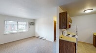 This single-floor unit offers a functional and straightforward layout designed for comfortable everyday living. The living area is generously sized, featuring neutral wall-to-wall carpeting that adds warmth underfoot. A window unit air conditioner and baseboard heating ensure year-round climate control, while a ceiling fan in the main living space promotes air circulation. Natural light filters in through windows that offer views of the surrounding neighborhood.

The galley-style kitchen is well-appointed with warm wood-toned cabinetry lining both walls, providing abundant upper and lower storage. Yellow laminate countertops lend a retro character to the space, which is equipped with a white electric coil range, a dishwasher, a refrigerator, and a stainless steel sink. A ventilation hood over the range and tile-style flooring complete the kitchen's practical design.

The full bathroom continues the consistent aesthetic with matching yellow countertops, a wood-toned vanity cabinet, a single-basin sink, a toilet, and a standard tub-shower combination. Tile flooring and a baseboard heater add comfort and functionality.

Throughout the unit, white walls and consistent finishes create a clean, cohesive atmosphere. The layout flows efficiently from the entry through the living space to the kitchen and bathroom, making practical use of the available footprint.