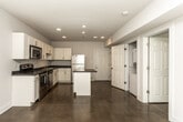 This single-floor unit is defined by its consistent use of polished concrete flooring throughout, lending the space a clean, modern industrial aesthetic. The open-concept kitchen serves as the functional centerpiece, featuring white shaker-style cabinetry that extends to the ceiling for ample storage, dark countertops, and a full suite of stainless steel appliances including a range, microwave, dishwasher, and refrigerator. A central kitchen island with a matching dark countertop provides additional workspace and casual seating potential. Recessed lighting illuminates the kitchen, complemented by a ceiling fan in the adjoining living area, which also benefits from a window fitted with horizontal blinds that admits natural light.

The bedrooms maintain the same polished concrete flooring and neutral white walls, each equipped with ceiling fans and windows that bring in natural light. The bathroom features a white vanity with modern hardware, a full soaking tub, and coordinating brushed nickel towel bars and fixtures. Throughout the unit, crisp white walls, clean lines, and a restrained color palette create a cohesive and functional living environment.