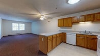Located along the Norwottoch Bicycle Path in Hadley, Massachusetts, this single-floor unit offers a practical and functional layout well-suited for everyday living. The open-concept design connects the kitchen and living area, creating a cohesive, spacious feel. The kitchen is well-appointed with warm oak cabinetry offering generous upper and lower storage, light-toned laminate countertops, a peninsula that defines the space, and white appliances including a refrigerator, electric range, dishwasher, and sink. Light vinyl flooring grounds the kitchen area, while a ceiling fan with integrated lighting serves the adjoining living space, which is finished with dark wall-to-wall carpeting.

The bedrooms are carpeted and finished with neutral walls, each featuring baseboard heating and windows that admit natural light and views of surrounding greenery. The layout includes a full bathroom equipped with a tub and shower surround and a wood-toned vanity, as well as a separate half bath with tile flooring and a grab bar. Baseboard heating is present throughout, ensuring year-round comfort. The overall design is straightforward and functional, with a neutral palette throughout.