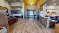 Located at 10520 Creek St SE in Yelm, Washington, this single-floor commercial space combines rustic lodge aesthetics with professional functionality. The grand entryway immediately sets the tone, featuring warm wood-look flooring, bold yellow ceiling accents, and a dramatic stacked-stone column that anchors the space. Elegant chandelier lighting adds a refined touch overhead.

The reception area is prominently positioned near the entrance, centered around a well-appointed front desk with wainscoted paneling and a granite countertop. Framed artwork and recessed lighting contribute to a polished yet welcoming atmosphere throughout.

Adjacent to the reception is a comfortable lounge area with soaring ceilings, a floor-to-ceiling stacked-stone fireplace with a mounted television, and plush leather seating arranged around a rustic wood coffee table. A kitchenette equipped with dark wood cabinetry, a refrigerator, microwave, and sink provides added convenience for staff or guests.

A second lounge or gathering area boasts dramatic vaulted ceilings with exposed wood beam detailing and large windows that flood the room with natural light while offering outdoor views. The space's cohesive use of natural stone, rich wood tones, and warm lighting throughout creates an inviting, upscale atmosphere well-suited for client-facing operations.