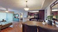 This single-floor residence offers a thoughtfully designed open-concept layout that seamlessly connects the living, dining, and kitchen areas. The living room features warm hardwood flooring, a ceiling fan, and a large sliding glass door that floods the space with natural light and provides access to the outdoors. A tufted leather sectional sofa and decorative accents complete the inviting atmosphere.

The kitchen is outfitted with rich dark espresso cabinetry, granite countertops, a breakfast bar peninsula, and a full suite of black appliances including a range, microwave, dishwasher, and refrigerator. The adjacent dining area accommodates a full-sized wooden table beneath a elegant pendant light fixture.

The bedrooms are carpeted and generously sized, each featuring ceiling fans, vertical blinds over large windows, and ample closet space. The primary bedroom includes an en-suite bathroom and a walk-in closet, while additional bedrooms offer comfortable layouts with stylish furnishings.

Throughout the unit, hardwood-style flooring runs through the main living areas, transitioning to plush carpet in the bedrooms. Textured ceilings and neutral warm-toned walls provide a cohesive backdrop, making this a functional and comfortable single-floor home.