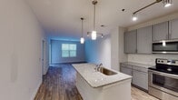 Located at 503 E Stone Ave in Greenville, SC, this single-floor unit offers a well-designed open-concept layout that seamlessly connects the kitchen, dining, and living areas. The kitchen is a standout feature, equipped with stainless steel appliances—including a refrigerator, range, and microwave—complemented by gray shaker-style cabinetry, a white subway tile backsplash, and a granite-topped island with a built-in sink and pendant lighting overhead. Track lighting adds additional illumination throughout the main living space, which features durable wood-style flooring that extends across the open layout. A built-in shelving nook adds functional character to the living area. The bedroom is carpeted and receives natural light through a window with views of surrounding greenery. The bathroom is finished with large-format tile flooring, a double-sink vanity topped with granite, gray cabinetry, a large mirror, and a tiled tub-shower combination. Throughout the unit, neutral tones, clean lines, and quality finishes create a cohesive, contemporary ambiance suited for comfortable everyday living.