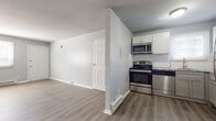 This single-floor unit offers a clean, functional layout with a thoughtful mix of finishes throughout. The open-concept living and kitchen area serves as the heart of the space, where durable hardwood-style flooring extends seamlessly underfoot. A ceiling fan overhead adds practical comfort to the living area, which flows directly into the kitchen via an open pass-through design.

The kitchen is well-appointed with a full suite of stainless steel appliances, including an electric range, over-the-range microwave, dishwasher, and refrigerator. White cabinetry provides ample storage, while a white subway tile backsplash and granite-style countertops add a polished, contemporary touch. A window above the sink allows natural light to brighten the workspace.

The bedroom features plush wall-to-wall carpeting and a generously sized walk-in closet with built-in shelving and rod, offering practical storage solutions. A window brings in natural light, creating a comfortable, quiet retreat.

The bathroom is finished with large-format neutral tiles surrounding the full bathtub and shower combination, complemented by wood-look tile flooring. Throughout the unit, light gray walls and white trim maintain a cohesive, modern aesthetic.