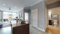 This thoughtfully designed single-floor residence offers a seamless open-concept layout that connects the kitchen, dining, and living areas into one cohesive space. The kitchen is equipped with dark espresso cabinetry reaching to the ceiling, granite countertops, stainless steel appliances including a gas range, built-in microwave, dishwasher, and a French door refrigerator, all complemented by a sleek tile backsplash and a peninsula with additional counter seating. Light hardwood-style flooring flows throughout the main living areas, accented by crown molding and soft gray walls that lend a refined, contemporary feel. The living room is bathed in natural light from floor-to-ceiling windows, offering outdoor views, and features a distinctive textured accent wall that adds visual depth and character. The bedroom is a tranquil retreat with plush carpeting, large windows framing green outdoor views, and elegant crown molding. A spacious walk-in closet with wire shelving connects directly to the full bathroom, which showcases granite-topped dual vanity cabinetry, stylish tile walls, and a full tub-shower combination. Throughout the residence, the interplay of natural light, modern finishes, and cohesive design elements creates a polished and comfortable living environment.