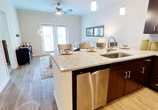 This 620 square foot apartment offers a thoughtful layout maximizing space and functionality. The open-concept design combines the kitchen and living areas, creating a sense of spaciousness. The kitchen boasts modern dark wood cabinetry, stainless steel appliances, and a granite countertop with a breakfast bar, perfect for casual dining or entertaining.

The living room features large windows allowing ample natural light, complemented by a ceiling fan for air circulation. Comfortable seating and a unique round coffee table create a welcoming atmosphere. The bedroom, measuring 180 square feet, includes a king-size bed, nightstands, and a ceiling fan, with plush carpeting for comfort underfoot.

The bathroom showcases a granite-topped vanity, large mirror, and a combination tub/shower with modern tile work. Wood-look flooring throughout the main living areas adds warmth and durability. Additional amenities include in-unit laundry and a private balcony or patio, accessible through glass doors, offering outdoor space for relaxation.

The apartment's neutral color palette and contemporary fixtures create a cohesive, stylish ambiance throughout. This efficient living space is ideal for those seeking a modern, low-maintenance lifestyle in a well-designed environment.
