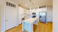 Located at 35205 Tupelo Cir in Frankford, Delaware, this single-floor, 2-bedroom, 2-bathroom home offers a clean, modern aesthetic throughout. The open-concept kitchen and living area serves as the heart of the home, showcasing crisp white shaker cabinetry extending to the ceiling, bright white countertops, stainless steel appliances including a French door refrigerator, range, microwave, and dishwasher, and a central island with pendant lighting above. Light wood-tone flooring runs throughout the main living areas, enhancing the airy, bright atmosphere. The living area features a ceiling fan and access to an exterior door with a transom window, inviting natural light. Both bedrooms are carpeted and equipped with ceiling fans, offering comfortable, quiet retreats. Multiple windows in each bedroom provide pleasant outdoor views and natural light. The primary bedroom includes a well-designed en-suite bathroom featuring a lengthy vanity with white cabinetry, a large mirror, and an adjacent walk-in closet with built-in shelving. A second full bathroom and a utility room add practicality to the layout. Five closets throughout the home ensure generous storage. The consistent use of white millwork, five-panel interior doors, and neutral tones gives the entire home a cohesive, contemporary feel.