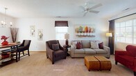Located at 2832 Starling St in Lima, Ohio, this single-floor residence offers a well-organized and cohesive living environment with a warm, inviting aesthetic carried throughout each room. The living area is generously proportioned, featuring plush carpeting, a ceiling fan, and natural light from windows dressed with decorative valances. A comfortable seating arrangement anchors the space, complemented by tasteful wall art and coordinated accent pieces. Adjacent to the living area, the dining space is defined by an elegant chandelier overhead and offers a welcoming setting for everyday meals or gatherings. The galley-style kitchen is efficiently laid out with rich wood cabinetry, light stone-toned countertops, tile flooring, and white appliances including a range, microwave, and refrigerator, providing ample storage and functionality. The bedroom is a restful retreat with soft carpeting, natural light filtering through curtained windows, and thoughtfully placed nightstands and accent mirrors that contribute to a calm atmosphere. The bathroom continues the warm wood cabinetry motif, featuring a single vanity with a wide mirror, tile flooring, and a separate shower enclosure. Together, these spaces create a practical and well-appointed single-level home.