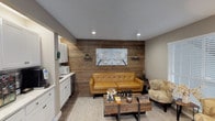 This single-floor commercial office space belonging to Karya is thoughtfully designed to blend professional functionality with a warm, inviting atmosphere. The layout flows seamlessly from a reception area near the entrance to a cozy lounge and a well-appointed kitchenette.

The reception area greets visitors with rich hardwood-style flooring, recessed lighting, and a branded entryway rug. French glass doors flood the space with natural light, while a large-screen display and a dedicated front desk create an organized and professional first impression.

Transitioning into the interior, a striking reclaimed wood accent wall serves as the centerpiece of the lounge area, adding rustic character and warmth. A tufted caramel leather sofa and patterned armchairs are arranged around a wooden coffee table, creating a comfortable and welcoming seating space. A window with blinds provides additional natural light, complemented by recessed ceiling lights.

The kitchenette is fully equipped with white shaker-style cabinetry, marble-look tile backsplash, a beverage refrigerator, a microwave, a sink, and a coffee station — offering guests and staff convenient refreshment options.

A connecting hallway features an exposed wood beam, a botanical gallery wall, and warm neutral tones that carry a cohesive design language throughout the entire space.