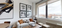 Located at 9 Livingston Ave in New Brunswick, NJ, this single-floor residence offers a thoughtfully designed modern interior with clean lines and contemporary finishes throughout. The open-concept layout connects the living, dining, and kitchen areas seamlessly, with light wood flooring running consistently across the main living spaces.

The kitchen is a standout feature, showcasing dark espresso cabinetry, stainless steel appliances, a glass tile backsplash, and generous counter space. A central island with seating provides an ideal spot for casual dining or entertaining. Recessed lighting illuminates the space efficiently.

The living area is bright and welcoming, benefiting from large windows that frame sweeping views of the New Brunswick skyline. Natural light fills the room, highlighting the clean white walls and contemporary furnishings.

The bedrooms continue the modern aesthetic, each featuring light wood floors, roller shades, and large windows offering elevated city views. The rooms provide a calm, restful atmosphere with ample space for furniture.

The bathroom maintains the contemporary design language with large-format tile flooring, a dark wood vanity with a clean white countertop, and a broad mirror. Overall, this residence presents a cohesive, urban-modern living environment in the heart of New Brunswick.