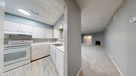 Located at 9110 Broadway in San Antonio, TX, this single-story 2-bedroom, 2-bathroom unit offers a practical and comfortable layout. The open living room is a standout space, featuring plush carpet flooring, neutral gray walls, a textured ceiling, and a corner fireplace with a raised brick hearth. Sliding glass doors lead directly to a private patio, filling the room with natural light and providing easy outdoor access.

The kitchen is well-appointed with white cabinetry, white countertops, a double-basin sink, and white appliances including a refrigerator, electric range, and dishwasher. Light wood-look flooring and a pass-through window connecting to the living area give the kitchen an open, functional feel.

Both bedrooms are carpeted and painted in soft gray tones with textured ceilings. The spacious primary bedroom features two windows that bring in natural light and includes a ceiling fan. The second bedroom offers generous space with ample wall area for flexible furniture arrangements.

The bathrooms are well-designed; one features a tub-shower combination with warm beige tile surround, while the other includes a clean vanity with white countertops, a framed mirror, and wood-look flooring. The overall aesthetic is neutral, clean, and move-in ready.