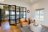 This single-floor amenity facility offers a thoughtfully designed collection of spaces that balance recreation, productivity, and comfort. The centerpiece is a spacious game room highlighted by a full-size pool table, a warm brick fireplace, wall-mounted displays, and a dramatic skylight that floods the area with natural light. Built-in shelving and a lounge seating nook add character and functionality to the space.

The fitness center is generously proportioned, outfitted with a comprehensive selection of cardio equipment including treadmills, ellipticals, and strength machines. Large windows along the perimeter invite natural light and offer outdoor views, while a colorful geometric carpet adds a modern, energetic feel underfoot.

Multiple office and workspace areas are distributed throughout the facility. Wide-plank hardwood flooring anchors these rooms, which feature clean white walls, recessed lighting, and ample desk configurations. A standout feature is a striking full-height natural stone accent wall that lends rustic warmth to one of the workspaces.

The lounge area provides an inviting retreat with leather and upholstered seating, a patterned area rug, and abundant natural light through large windows. A set of elegant black-framed glass folding doors connects the lounge to an adjoining stone-accented dining or conference space, creating a seamless, sophisticated flow throughout the facility.