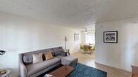 This single-floor residence offers a thoughtfully designed layout that balances comfort and functionality throughout. The living area is bright and welcoming, featuring light hardwood-style flooring, a textured ceiling, and windows fitted with horizontal blinds that allow natural light to filter in. The space flows seamlessly into a dedicated dining nook, where a ceiling fan overhead and a window to the exterior create an airy, intimate setting ideal for everyday meals.

The kitchen is outfitted with light grey shaker-style cabinetry, a white subway tile backsplash, and a full suite of stainless steel appliances including a gas range, over-the-range microwave, and refrigerator. A white countertop island provides additional prep space, while a window brings in natural light.

The primary bedroom is generously sized, offering a walk-in closet, a ceiling fan with integrated lighting, and a window with views of mature trees outside. The second bedroom mirrors this layout with its own ceiling fan and ample natural light. Both rooms feature the same light wood-style flooring found throughout the home.

The bathroom is clean and functional, with a white subway tile tub surround, a pedestal sink, a framed mirror, and a small window for ventilation. The entry area provides a welcoming transition into the home, complete with hardwood-style floors and a bright window.