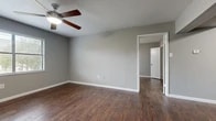 This single-story space offers a practical and cohesive interior design carried consistently throughout its rooms. Dark hardwood-style flooring runs through the living areas, bedrooms, kitchen, and bathroom, creating a unified aesthetic that contrasts with the neutral gray walls and crisp white trim. Textured ceilings add architectural character, while ceiling fans with integrated lighting are installed in the main living area and bedrooms, supporting both comfort and airflow.

The living area serves as the entry point to the unit, featuring a front door flanked by a window fitted with horizontal blinds that allows natural light to filter in. The kitchen is a standout space, appointed with dark espresso cabinetry, granite-patterned countertops, a stainless sink, and black appliances including a range and refrigerator, offering a bold, contrasting palette.

The bedrooms are generously sized, each benefiting from natural light via windows and ceiling fans. One bedroom includes an adjoining closet with a rod and direct access to a full bathroom, which features a tub-shower combination with white tile surround and matching fixtures. A dedicated laundry area accommodates a full-size washer and dryer. The layout flows efficiently, with clear sightlines and well-defined spaces throughout.
