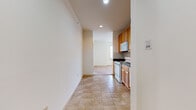 This single-floor unit offers a practical and comfortable layout with clearly defined living areas. The kitchen is well-appointed with warm honey-toned wood cabinetry, dark granite-style countertops, a subway tile backsplash, and white appliances including a range, over-the-range microwave, and dishwasher. Large-format tile flooring extends through the kitchen and into the connecting hallway, providing a clean and durable surface underfoot.

The bedrooms are carpeted in a neutral tone and feature individual wall-mounted PTAC heating and cooling units, ensuring independent climate control. Windows fitted with horizontal blinds allow natural light to filter in while maintaining privacy. One bedroom benefits from a ceiling fan for added comfort and air circulation.

The bathroom is finished with the same tile flooring found in the kitchen, complemented by a wood-framed vanity with a dark granite-style countertop and an integrated sink. A shower-tub combination with a curtain rod completes the space.

The overall layout, as visible in the dollhouse view, connects the kitchen to the living and bedroom areas in a straightforward flow. Neutral cream-toned walls throughout create a bright, clean ambiance well-suited for a variety of uses.