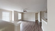 This single-floor residence offers a clean, modern aesthetic defined by warm neutral tones, crisp white trim, and durable wood-style flooring that flows consistently throughout the main living areas. The open-concept layout connects the living room to the kitchen seamlessly, with crown molding accenting the transition and a peninsula counter providing both workspace and a natural visual divider. The living area is generously proportioned, bathed in natural light through vertical-blind-covered windows, and finished with a stylish ceiling fan overhead.

The kitchen is equipped with stainless steel appliances—including a refrigerator, range, and microwave—set against dark cabinetry and light countertops, with tile flooring underfoot. Multiple bedrooms are present throughout the unit, each featuring the same wood-style flooring, ceiling fans, and windows with vertical blinds that allow for adjustable natural light. The rooms offer a versatile, move-in-ready canvas.

The bathrooms include full tub-shower combinations with white tile surrounds, complemented by dark tile flooring that adds contrast to the neutral walls. Throughout the space, consistent design choices—neutral paint, white doors, and clean finishes—create a cohesive and functional living environment suitable for a range of lifestyles.