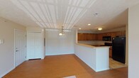 This single-floor unit offers a practical and functional layout designed to maximize living comfort. The main living area greets occupants upon entry, featuring warm hardwood-style flooring and a decorative chandelier overhead. A textured ceiling adds dimension to the space, while recessed lighting provides even illumination throughout. A half-wall peninsula visually separates the living area from the kitchen, creating an open-concept flow without sacrificing definition between spaces.

The kitchen is well-appointed with medium-toned wood cabinetry extending both above and below generous countertops, offering substantial storage and workspace. Black appliances, including a gas range, built-in microwave, and refrigerator, are integrated seamlessly. Tile flooring grounds the kitchen area practically.

The bedrooms are carpeted for comfort and feature neutral walls. One bedroom notably includes two side-by-side closets with bi-fold doors, while a second bedroom offers a single closet, each providing solid storage capacity. Natural light filters into the bedrooms through windows, with one room offering an exterior view of the surrounding landscape.

The bathroom includes a vanity with wood cabinetry, a single sink, a toilet, and a shower-tub combination with a curtain rod. Tile flooring completes the functional design.

The living area also features a sliding glass door that opens to an outdoor view, allowing natural light to brighten the carpeted lounge space.