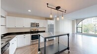 Located at 1214 Griswold St in the heart of downtown Detroit, this one-bedroom, one-bathroom unit offers a well-designed layout across a single floor. The living room is an immediate standout, anchored by a dramatic floor-to-ceiling arched window that floods the space with natural light and frames sweeping views of the surrounding cityscape, including nearby landmarks and green spaces. The herringbone-patterned hardwood flooring flows seamlessly throughout, adding a refined, classic touch to the modern interior. The kitchen is well-appointed with crisp white shaker cabinetry, dark granite countertops, stainless steel appliances including a range, microwave, and refrigerator, and an industrial-style mobile island with a stainless steel top beneath striking pipe-and-pendant lighting. The bedroom offers a comfortable and private retreat, with the same herringbone flooring and generous proportions. A dedicated closet provides ample storage. The hallway connects the rooms with clean lines and neutral tones, maintaining a cohesive aesthetic throughout. The bathroom is fitted with white tile flooring, a glass-enclosed walk-in shower, and built-in wire shelving for added convenience. This unit combines historic architectural character with contemporary upgrades in a prime Detroit location.