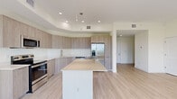 Located at 8510 W 40th Ave in Hialeah, FL, this well-designed two-story home offers 3 bedrooms and 2 bathrooms across two thoughtfully laid-out floors. The main level features an open-concept living room and kitchen bathed in natural light, with large sliding glass doors that frame lush outdoor greenery and invite the Florida sunshine indoors. Light wood-tone flooring flows seamlessly throughout, complementing the home's bright, neutral color palette. The kitchen is a standout, showcasing floor-to-ceiling wood-grain cabinetry, a tray ceiling with recessed and pendant lighting, a generous center island with a clean quartz-style countertop, and a full suite of stainless steel appliances. The upper floor hosts the three bedrooms, including a spacious primary bedroom with an en-suite bathroom and a dedicated closet featuring built-in wire shelving. The bathrooms are finished with warm wood vanities, backlit LED mirrors, and clean tile work. Dual staircases connect the floors, and a dedicated garage with an automatic opener provides secure parking and additional storage. The home's crisp white walls, modern finishes, and abundance of natural light throughout create a clean, contemporary atmosphere.