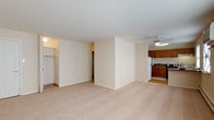 This single-floor residence offers a practical and comfortable layout designed for everyday living. The main living area is generously sized, featuring neutral-toned wall-to-wall carpeting that creates a warm, cohesive atmosphere throughout. A ceiling fan overhead adds both function and airflow to the space. A large walk-in closet off the living area provides ample storage, while the open layout allows for flexible furniture arrangements.

The kitchen is situated adjacent to the living area and is equipped with warm-toned wooden cabinetry offering abundant upper and lower storage. Dark laminate countertops contrast neatly with the cabinetry, and the space includes a full suite of appliances: a white refrigerator, electric range, dishwasher, and a stainless steel sink. Light hardwood-style flooring in the kitchen distinguishes it from the carpeted living spaces.

The bedroom is a well-proportioned room with soft carpeting, a window that brings in natural light, and a closet with bi-fold doors. Baseboard heating runs along the walls, ensuring warmth throughout the colder months.

The bathroom is finished in a clean, all-white palette, featuring white square tile in the tub surround, tile flooring, a single-sink vanity with a mirror cabinet, and a full bathtub with shower.
