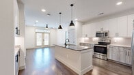 This well-appointed 2-bedroom, 2-bathroom single-story residence offers a thoughtfully designed open-concept layout. The kitchen serves as the heart of the home, showcasing a large center island with a dark granite countertop and integrated sink, stainless steel appliances including a range, microwave, and refrigerator, and a combination of white and wood-toned cabinetry accented by a tiled backsplash. Pendant lighting overhead adds a modern touch. The kitchen flows seamlessly into the living area, which features rich hardwood-style flooring, recessed lighting, a ceiling fan, and French doors that open to a private balcony, inviting an abundance of natural light.

Both bedrooms are carpeted and offer a warm, comfortable feel, with natural light provided by windows fitted with blinds. The primary bedroom includes a ceiling fan and is served by an en-suite bathroom featuring a dual-sink granite vanity with wood-toned cabinetry, black matte fixtures, and a backlit mirror. A spacious walk-in closet with built-in shelving and hanging rods provides ample storage. A second closet serves the additional bedroom. Throughout the residence, five-panel interior doors with matte black hardware lend a clean, contemporary aesthetic that ties the entire space together cohesively.