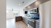 This thoughtfully designed one-bedroom, one-bathroom residence offers a cohesive open-concept layout that seamlessly connects the kitchen and living room, creating a functional and inviting living space. The kitchen is a standout feature, showcasing gray shaker-style cabinetry, granite countertops, a striking deep-blue subway tile backsplash, and a full suite of stainless steel appliances including a range, microwave, dishwasher, and refrigerator. A peninsula with additional counter space enhances both storage and functionality. Light wood-tone flooring runs throughout the main living areas, contributing to a clean, contemporary aesthetic. The living area is brightened by natural light from large windows and is equipped with a ceiling fan for added comfort. The bedroom offers plush carpeting, multiple windows with outdoor views, a ceiling fan, and direct access to a dedicated walk-in closet with built-in shelving and hanging rods. The bathroom features a soaking tub with white tile surround accented by decorative navy blue penny tile border details and coordinating floor tile, delivering a polished, modern finish. The overall design emphasizes clean lines, cohesive finishes, and practical living.