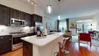 This single-story residence offers a thoughtfully designed open-concept floor plan that seamlessly connects the kitchen, dining, and living areas. The kitchen is a standout feature, equipped with dark espresso cabinetry reaching toward the ceiling, stainless steel appliances, a tile backsplash, granite countertops, and a generous island with a bright white quartz surface and bar seating. Pendant lighting adds a contemporary touch overhead, while warm hardwood flooring flows throughout the main living areas.

The living room is bright and inviting, with large sliding glass doors that open to a private balcony overlooking lush greenery, filling the space with natural light. The two bedrooms are comfortably scaled, each featuring plush carpeting, large windows with outdoor views, and ceiling fans for added comfort.

Both bathrooms are finished with marble-style tile, offering an elegant aesthetic. The primary bathroom includes a glass-enclosed shower and a granite-topped vanity, while the second bathroom features a soaking tub with full marble tile surround. Together, these spaces combine modern finishes with a warm, livable atmosphere throughout.