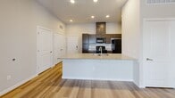 Located at 1100 Avenida Mercado Street in Manchaca, TX, this single-story, three-bedroom, two-bathroom home offers a well-designed layout with modern finishes throughout. Light wood-look flooring flows seamlessly across all living areas, creating a bright and cohesive aesthetic.

The open-concept kitchen serves as the heart of the home, anchored by a peninsula island with a granite countertop and an undermount sink. Dark espresso cabinetry provides ample storage and contrasts elegantly with the light granite surfaces. Black appliances, including a range, microwave, refrigerator, and dishwasher, complete the kitchen. Recessed lighting and a ceiling fan enhance the living area, which opens toward a glazed exterior door for added natural light.

The three bedrooms are finished with the same wood-look flooring and feature windows with blinds that bring in natural light. Ceiling fans are present in the bedrooms for comfort. The two closets are generously sized walk-ins, each outfitted with multi-tiered wire shelving systems for organized storage.

The bathrooms are finished with granite-topped dark vanities. One bathroom includes a full soaking tub and shower combination, with direct access to a walk-in closet. A connecting hallway links the private bedroom wing to the main living areas, maintaining a clear and functional floor plan throughout.