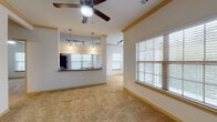 Located along SH-151 in San Antonio, Texas, this single-story unit offers a well-organized, open-concept floor plan designed for comfortable everyday living. The main living area is generously proportioned, finished with warm-toned carpeting, crown molding, and a ceiling fan with integrated lighting. Multiple windows fitted with horizontal blinds allow natural light to fill the space while providing privacy, and track lighting adds additional illumination throughout.

The kitchen is a functional highlight, featuring rich dark-wood cabinetry extending to the ceiling for ample storage, granite-look countertops, and a full suite of black appliances including a refrigerator, range, microwave, and dishwasher. Wood-look flooring runs through the kitchen, and a pass-through counter with pendant lighting connects the kitchen to the living area, enhancing the open feel of the layout. A window above the sink brings in natural daylight.

The bedrooms continue the carpeted flooring and include ceiling fans and windows with outdoor views. The bathrooms are finished with wood-look flooring, rich wood-toned cabinetry, granite-look countertops, and white-tiled tub-shower combinations, offering a clean and cohesive aesthetic throughout the unit.