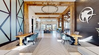 Located at 3144 Old Franklin Rd in Antioch, TN, this expansive single-story clubhouse blends rustic charm with modern sophistication across a generously sized, open-concept floor plan. The architectural design is defined by dramatic soaring ceilings adorned with exposed reclaimed wood beams and trusses, complemented by large-format herringbone-patterned tile flooring and floor-to-ceiling steel-framed windows that flood the interior with natural light and frame outdoor views.

The main gathering area serves as the heart of the space, featuring live-edge wood communal tables, plush velvet seating, and statement candle-style chandeliers. A dedicated lounge area offers comfortable sectional seating, leather sofas, and a striking dark wood accent wall with bold X-pattern detailing, alongside a billiards table for recreation. A cozy window seat with built-in firewood storage overlooks an outdoor terrace and lush landscape views.

A secondary lounge provides an intimate retreat with floor-to-ceiling corner windows, curated artwork, a wall-mounted TV, and a small built-in dining nook. The space also includes a wet bar area with a vibrant geometric tile backsplash and a coffee station. The hallway connects the areas seamlessly, while the overall ambiance balances warmth and energy, making it an inviting, multi-functional communal destination.