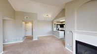 This single-floor residence is designed with an open, airy layout accentuated by soaring vaulted ceilings that lend a sense of generous volume throughout the main living areas. The living room serves as a central gathering space, anchored by a fireplace with a white mantel and flanked by built-in shelving units. Large arched windows flood the room with natural light while providing outdoor views, and a glass-paned door opens directly to a private balcony. Neutral-toned carpet and warm gray walls create a cohesive, understated aesthetic.

The kitchen is thoughtfully designed with dark espresso cabinetry, light granite countertops, a double undermount sink, and stainless steel appliances including a refrigerator and over-the-range microwave. A peninsula counter offers additional workspace and connects the kitchen to the living area. Wood-look flooring grounds the kitchen and extends through the wet areas.

The bedroom features vaulted ceilings, a ceiling fan, built-in shelving, ample natural light from a sizable window, and a walk-in closet. Two bathrooms are present: one with a granite-topped vanity, dark cabinetry, a framed mirror, and a tiled shower, and a second with a glass-enclosed shower stall and matching granite vanity finishes.