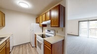 This single-floor, 2-bedroom, 1-bathroom space offers a well-organized and functional layout designed for efficient everyday living. The galley-style kitchen is a standout feature, lined on both sides with warm oak cabinetry offering generous storage, light-toned countertops, a double-basin sink, and white appliances including an electric range and refrigerator. Light wood-look flooring runs through the kitchen and hallway, adding a clean, cohesive aesthetic throughout the common areas. The central hallway connects all rooms seamlessly, with multiple doors providing access to the bedrooms, bathroom, and storage closets. The primary bedroom is notably spacious, featuring plush carpet, two closets — including a full bi-fold — and ample room for furnishings. The second bedroom is more compact but equally well-appointed, with carpet flooring, a ceiling light fixture, and a window that invites natural light. The bathroom is clean and straightforward, equipped with a full-size soaking tub and shower combo featuring a white surround with built-in shelving and chrome fixtures. Throughout the space, neutral wall tones, textured ceilings, and dark wood door and baseboard trim provide a consistent, understated design language.