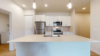 Located in Phoenix, AZ, this well-appointed 2-bedroom, 2-bathroom residence offers a clean, modern aesthetic throughout its single-story layout. The open-concept kitchen and living area serves as the heart of the home, featuring a large quartz-topped island with an undermount sink, white shaker cabinetry, a tiled backsplash, and a full suite of stainless steel appliances including a refrigerator, electric range, and microwave. Pendant lighting above the island adds a contemporary touch. Light wood-style flooring runs consistently throughout the space, enhancing the bright, airy feel created by recessed lighting and neutral wall tones. The primary bedroom is generously sized and connects to a private balcony via sliding glass doors, allowing for natural light and outdoor access. Each bedroom is equipped with a ceiling fan and window with blinds. The two bathrooms are thoughtfully designed, with the primary bath offering a dual-sink vanity with quartz countertops and a glass-enclosed walk-in shower. Both bedrooms feature dedicated walk-in closets with built-in shelving and hanging rods. A dedicated laundry room houses a full-size washer and dryer. The overall ambiance is contemporary, clean, and functional — well-suited for comfortable everyday living.