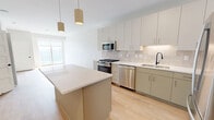 Located at 3130 Monterey Avenue South in Minneapolis, MN, this one-bedroom, one-bathroom unit offers a thoughtfully designed open-concept layout with clean, modern finishes throughout. Light wood flooring flows seamlessly across the entire space, complementing the crisp white walls and creating a bright, cohesive aesthetic.

The combined kitchen and living area forms the heart of the unit. The kitchen is well-appointed with stainless steel appliances, including a gas range, microwave, dishwasher, and refrigerator. Taupe flat-front cabinetry lines the walls with ample upper and lower storage, while a tiled backsplash adds texture. A central island with a white quartz countertop provides additional prep space and serves as a natural gathering point. Pendant lighting above the island adds warmth and style.

The living area benefits from large sliding glass doors that flood the space with natural light and offer views of the surrounding neighborhood. The bedroom is a comfortable retreat with a dedicated window providing additional natural light and outdoor views. It includes direct access to a spacious walk-in closet outfitted with multi-tiered wire shelving for generous storage capacity.

The bathroom features a taupe vanity with a white countertop, a framed mirror, and clean, neutral finishes consistent with the rest of the unit.