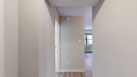 This efficiently designed one-bedroom, one-bathroom unit offers a thoughtful layout across a single floor, making smart use of every square foot. The entry hallway, finished with light hardwood-style flooring and clean white walls, leads seamlessly into the main living areas. The spacious bedroom is the largest room in the unit, featuring warm hardwood-style flooring, neutral gray-toned walls, and a window with views of the surrounding urban streetscape. A wall-mounted HVAC unit provides climate control, while baseboard heating adds supplemental warmth. The kitchen is well-equipped with a full suite of stainless steel appliances, including a refrigerator, electric range, over-the-range microwave, and dishwasher. Gray shaker-style cabinetry with ample upper and lower storage lines the walls, complemented by a clean white countertop, a modern sink with a black gooseneck faucet, and a subtle tile backsplash. Track lighting overhead illuminates the workspace efficiently. The bathroom features a contemporary floating vanity with wood-toned cabinet doors, a mirrored medicine cabinet, a full-size bathtub with an overhead rain showerhead, and white subway tile surround. Gray floor tiles and bright overhead lighting complete the clean, modern aesthetic throughout.